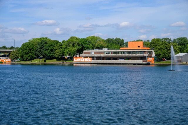 Lakeside building near water in Plumstead, London, with lush green trees and a fountain, offering sc.