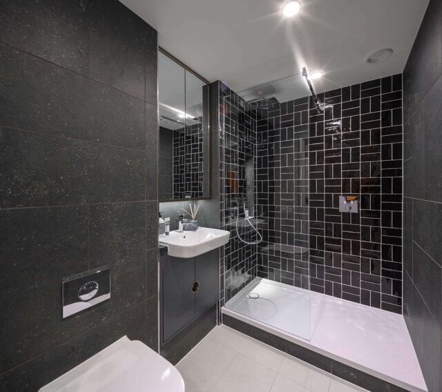 Modern bathroom with black tiled walls and walk-in shower in London apartment.