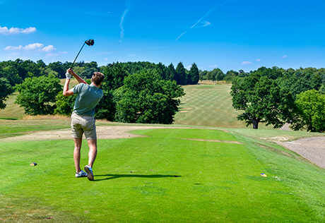Man playing golf on lush green course near historic Enfield houses.