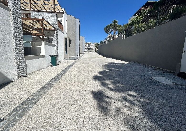 Gated complex street in Bodrum with paved road, modern villas, and private beach access nearby.