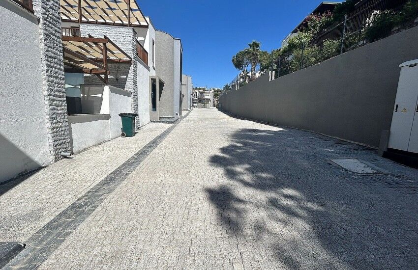 Gated complex street in Bodrum with paved road, modern villas, and private beach access nearby.