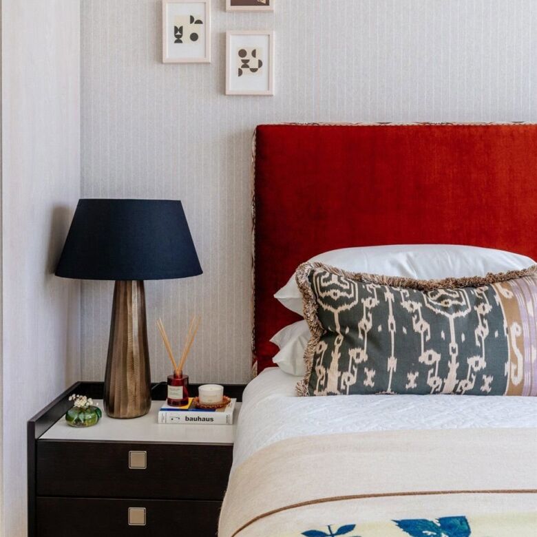 Modern bedroom with red headboard, black bedside table, and abstract wall art.