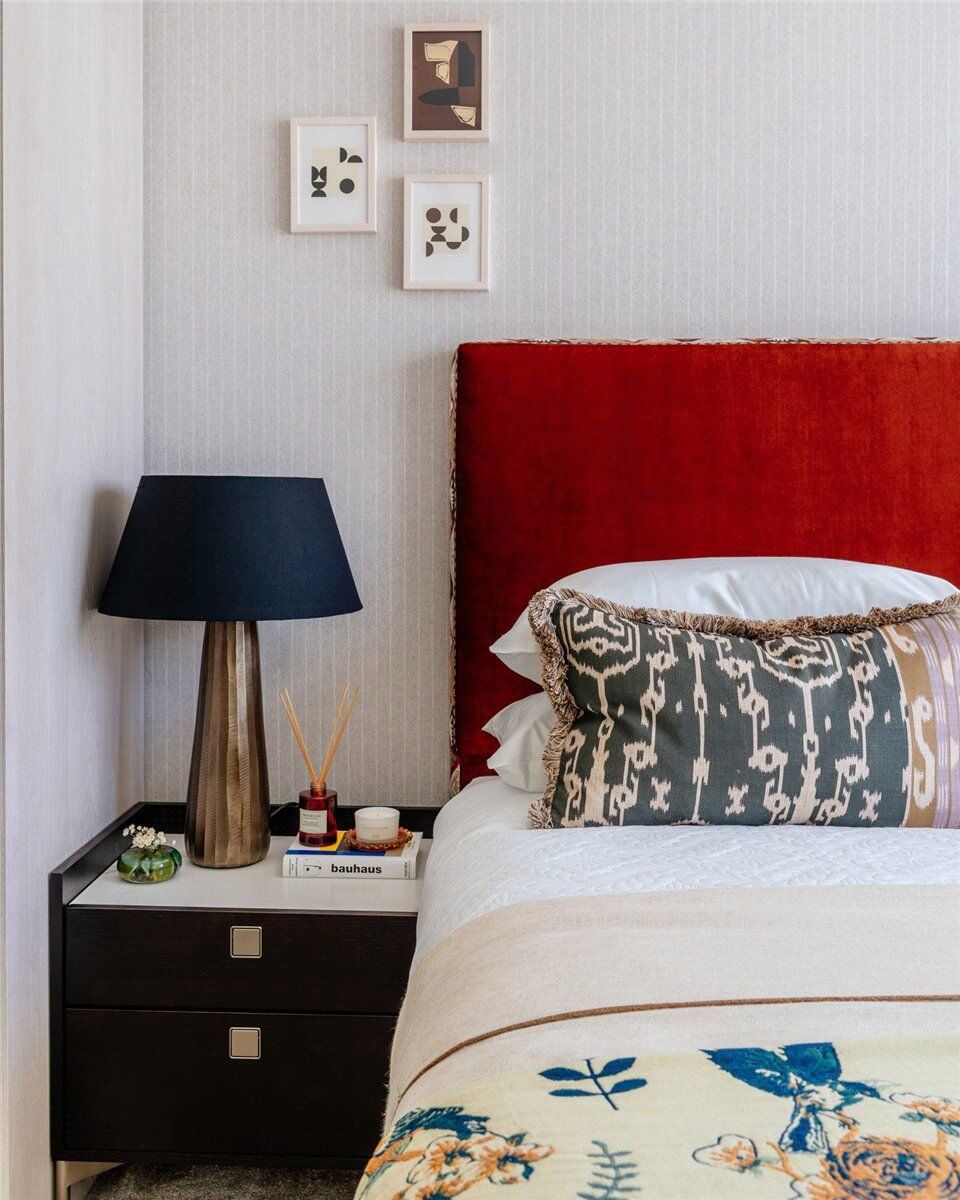 Modern bedroom with red headboard, black nightstand, and contemporary wall art.