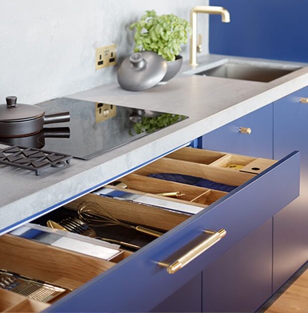 Blue kitchen cabinets with open drawers showing utensils and cutlery.