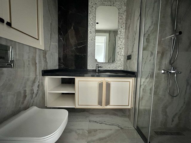 Bright modern bathroom with marble tiles and a glass shower enclosure in Alanya.