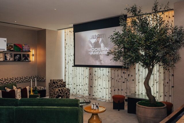 Stylish lounge with a large screen, cozy seating, and a potted tree in a riverside apartment.