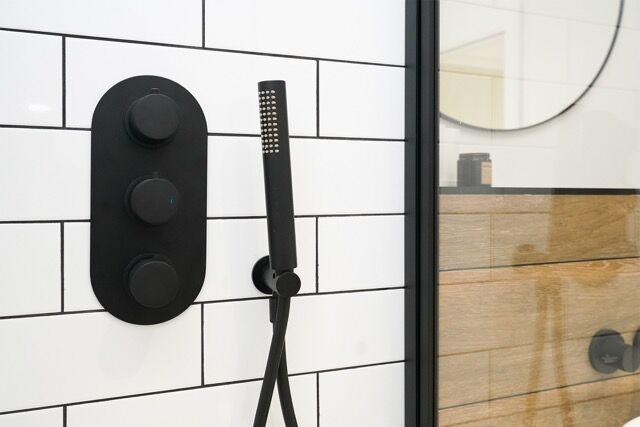 Modern shower head with black controls in a contemporary bathroom setting.