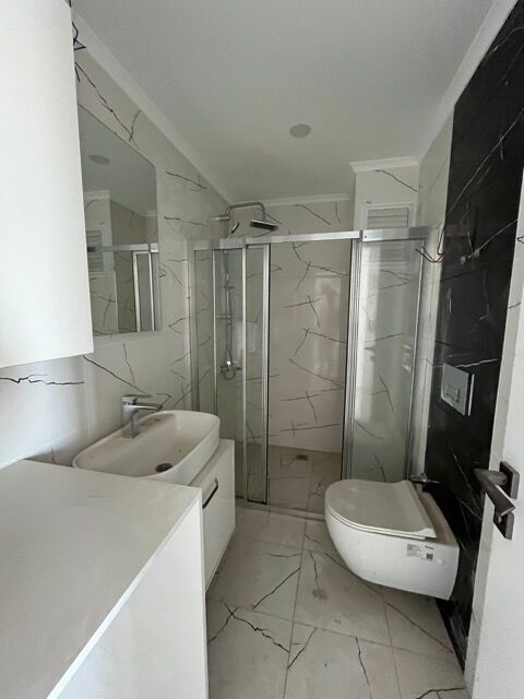 Modern 1-bedroom apartment bathroom with shower, toilet, and sleek design in Alanya.