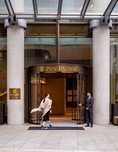 Elegant entrance of Pan Pacific London hotel with modern glass facade and welcoming staff.