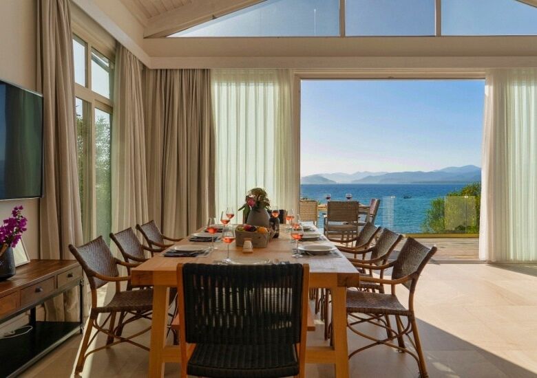 Seafront villa dining room with large windows overlooking the sea and mountains, featuring a wooden.