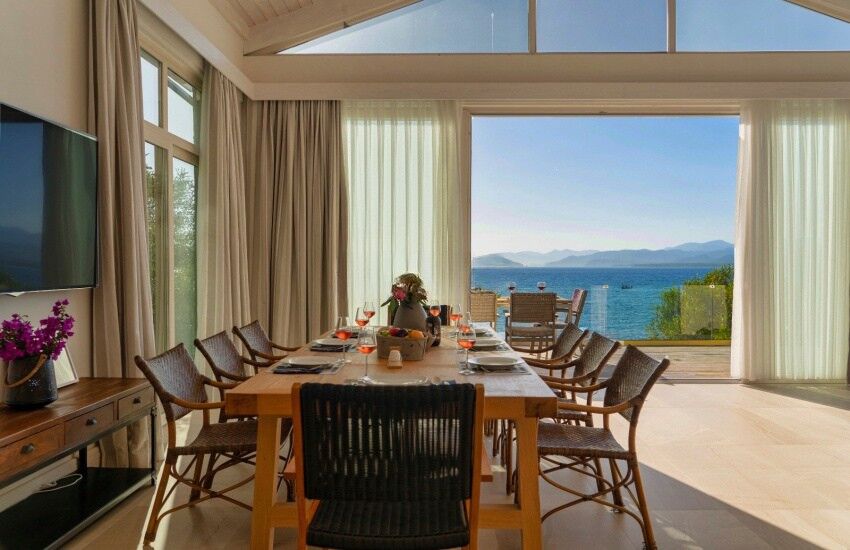 Seafront villa dining room with large windows overlooking the sea and mountains, featuring a wooden.