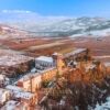 Castle in Piedmont with snow-covered landscape and rolling hills.