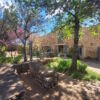 Beautiful stone house with lush garden, mature trees, and a swimming pool in a scenic rural setting.