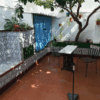 Outdoor courtyard with tiled walls, a small table, and chairs under a tree.