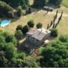 Elegant countryside villa in Tuscia Viterbo surrounded by lush greenery and tall cypress trees.