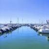 Marina with boats and yachts docked in El Perello Tarragona harbor under clear blue sky.