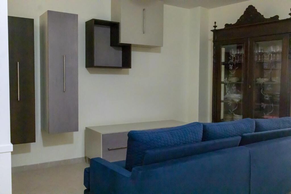 Modern Living Room with Blue Sofa and Wall Shelves Modern living room featuring a blue sofa, wall-mounted shelves, and a classic wooden display cabinet.