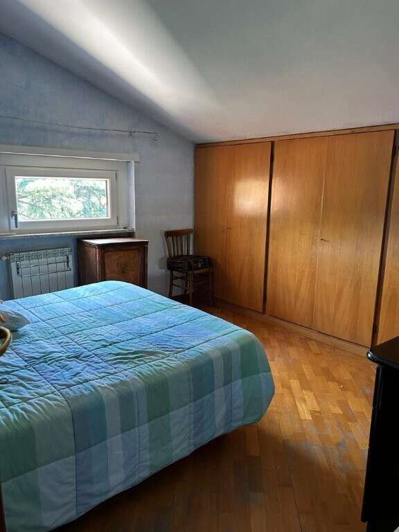 Bedroom with wooden wardrobe and window in Ariccia Rome penthouse apartment.