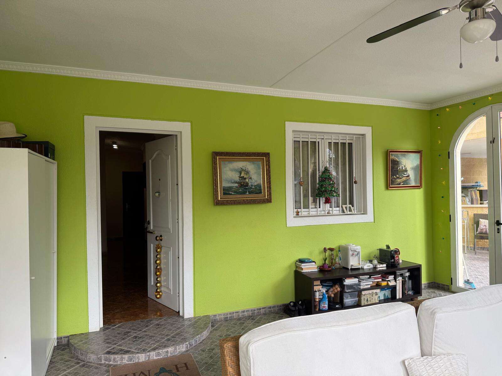 Bright living room with green walls, white furniture, and large windows in a villa for sale in El Ca.