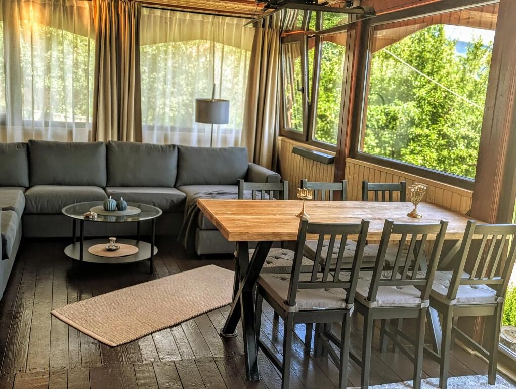 Bright living room with large windows overlooking lush greenery, featuring a comfortable sofa and a.