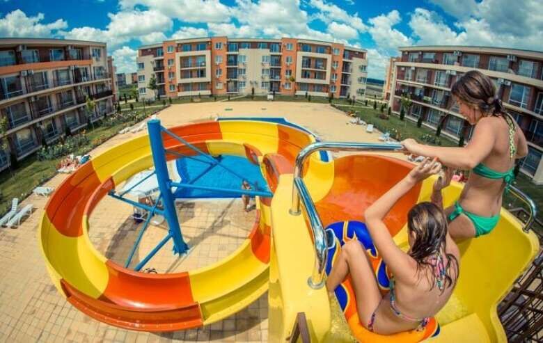 Bright poolside scene at Holiday Fort Club with children enjoying water slide.