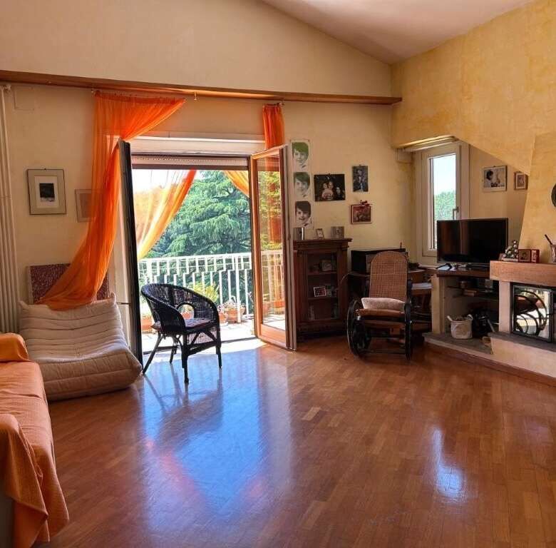Bright living room with balcony overlooking greenery, fireplace, and comfortable seating.
