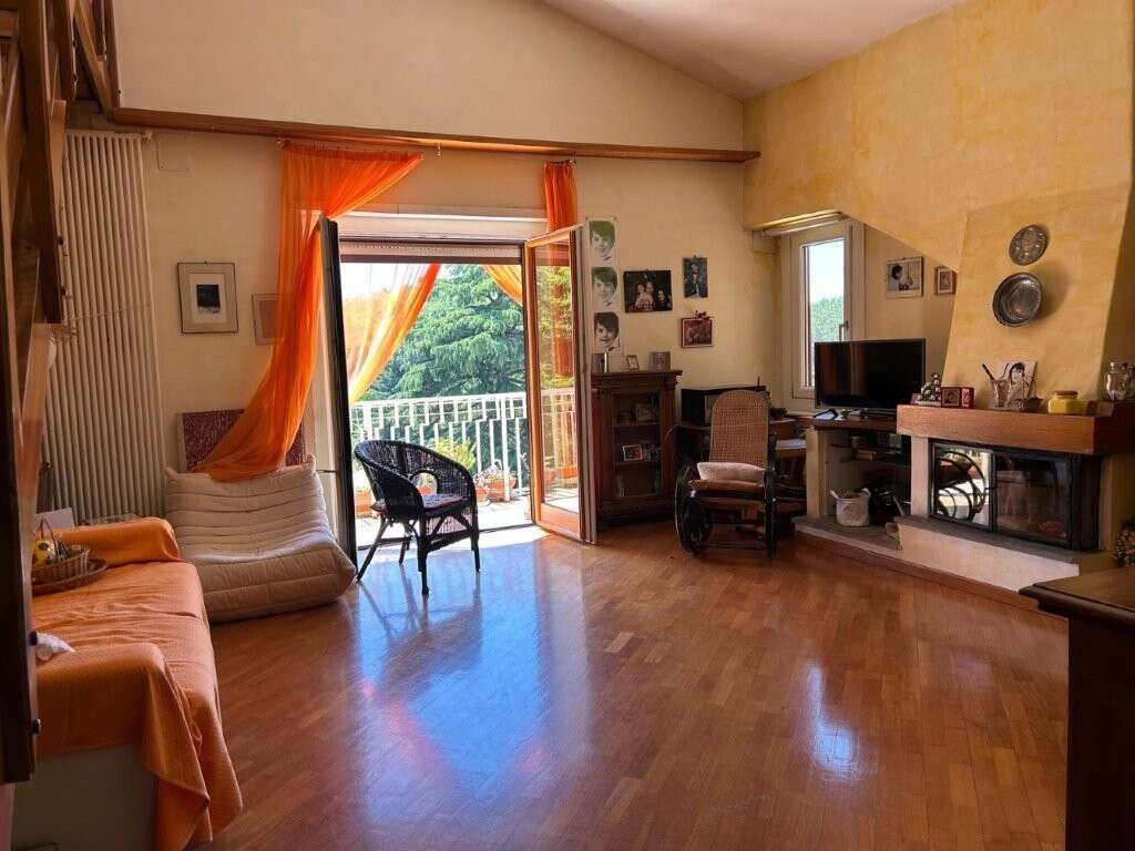 Bright living room with balcony overlooking greenery, fireplace, and comfortable seating.