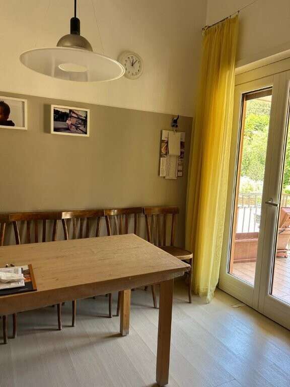 Bright dining space with wooden table and chairs, large glass door leading to balcony, and yellow cu.