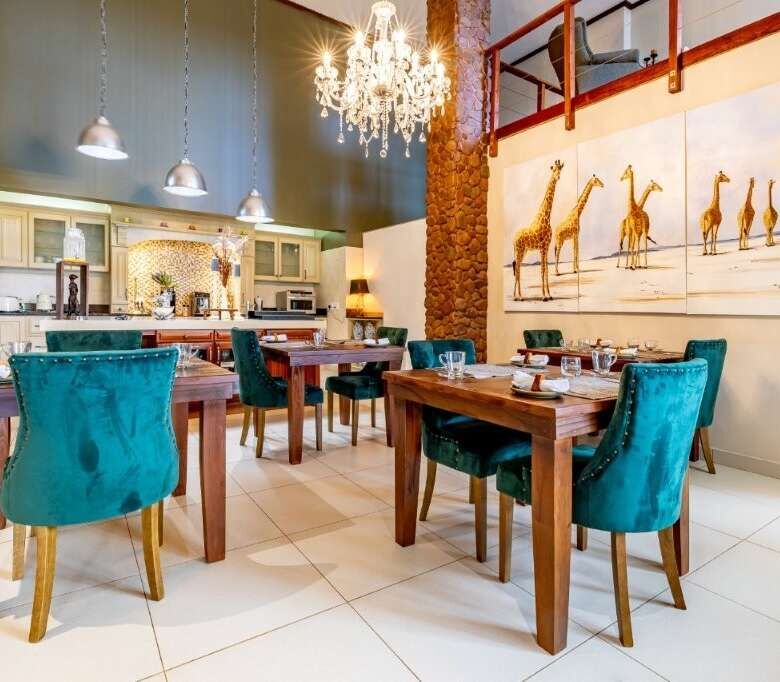 Elegant dining room featuring a chandelier, wooden tables, and vibrant teal chairs, with large giraf.