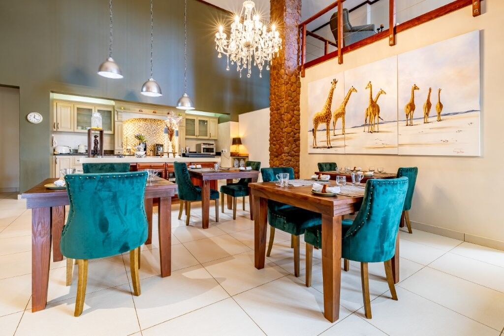 Elegant dining room featuring a chandelier, wooden tables, and vibrant teal chairs, with large giraf.