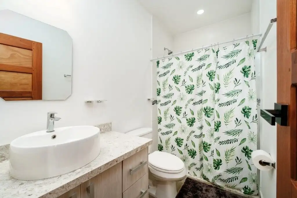 Condo bathroom with white fixtures and tropical leaf shower curtain in Pedasi.