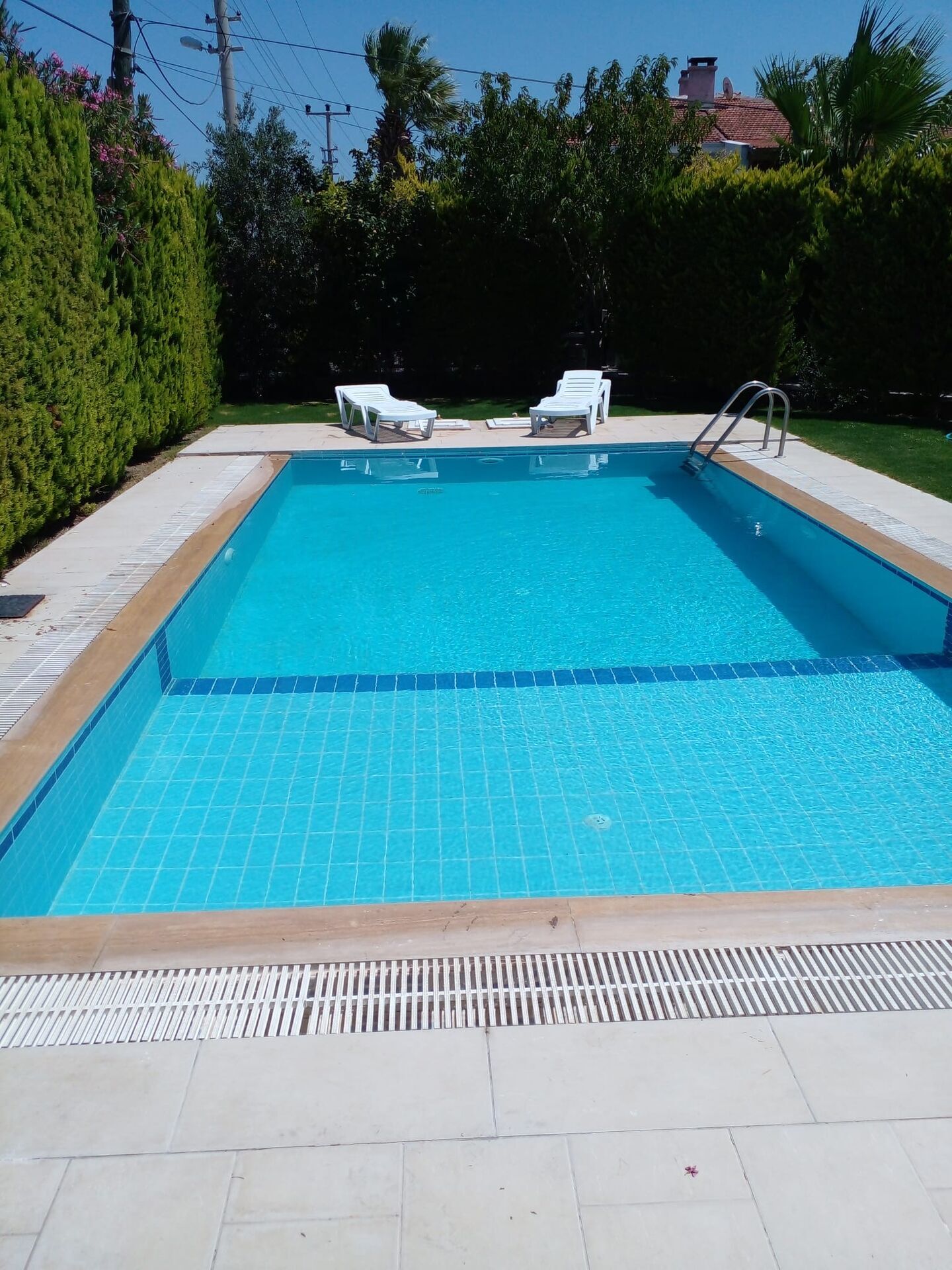 Luxury 3 Bed Villa Pool in Cesme Pool area of a luxury 3-bedroom villa in Cesme with clear blue water and surrounding greenery.