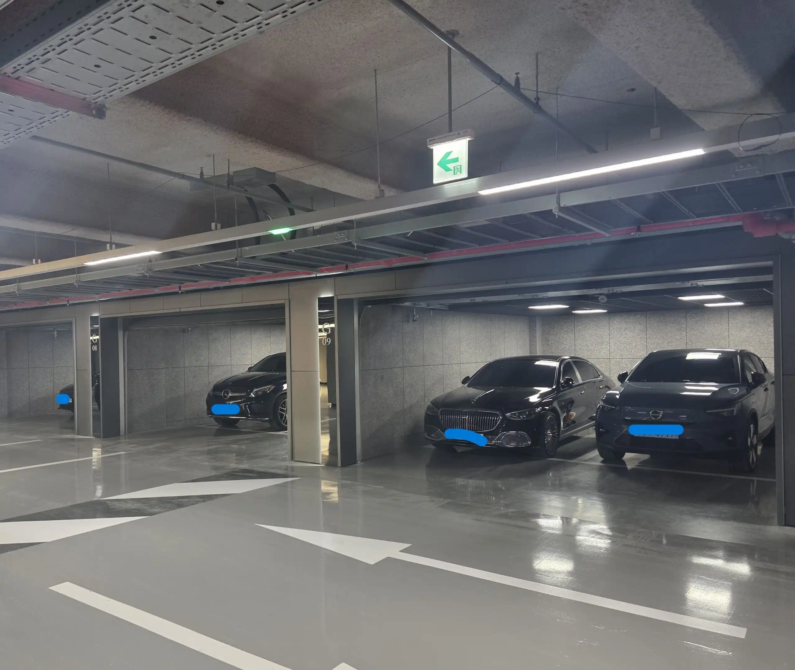 Modern underground parking with sleek black cars and clear signage.