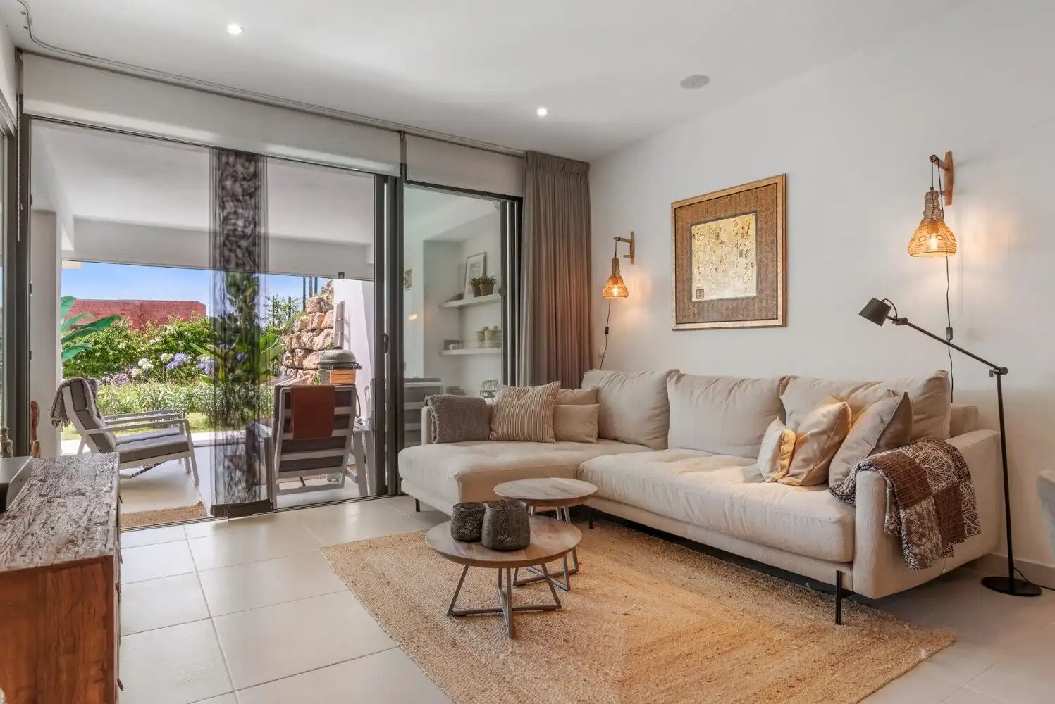 Bright and spacious living room with sliding glass doors leading to a balcony and outdoor seating ar.