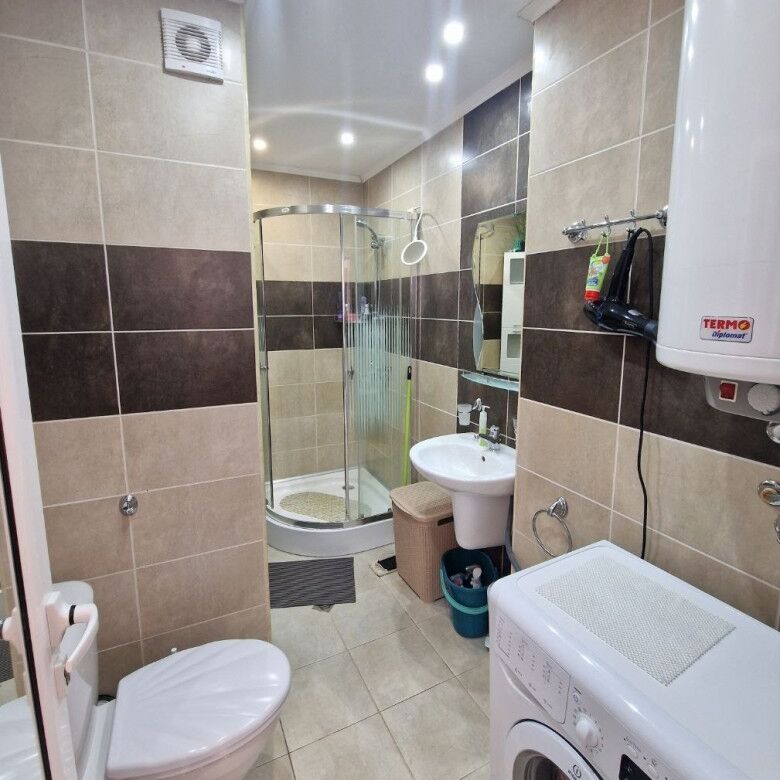 Bright bathroom featuring a shower enclosure, toilet, sink, and laundry appliances.
