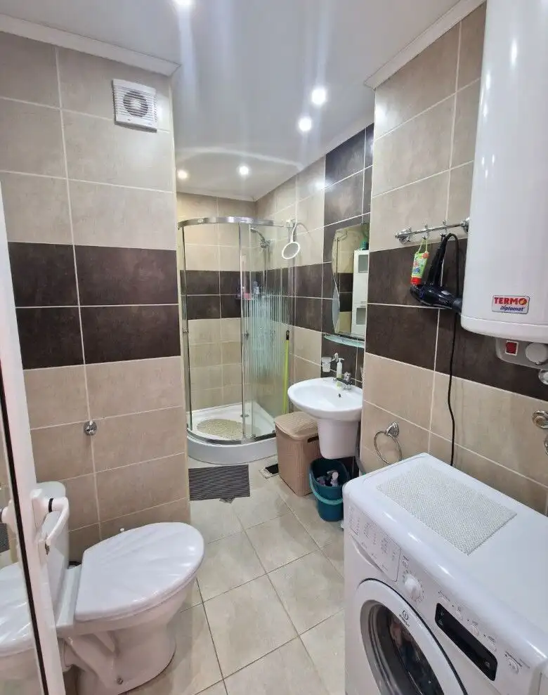 Bright bathroom featuring a shower enclosure, toilet, sink, and laundry appliances.