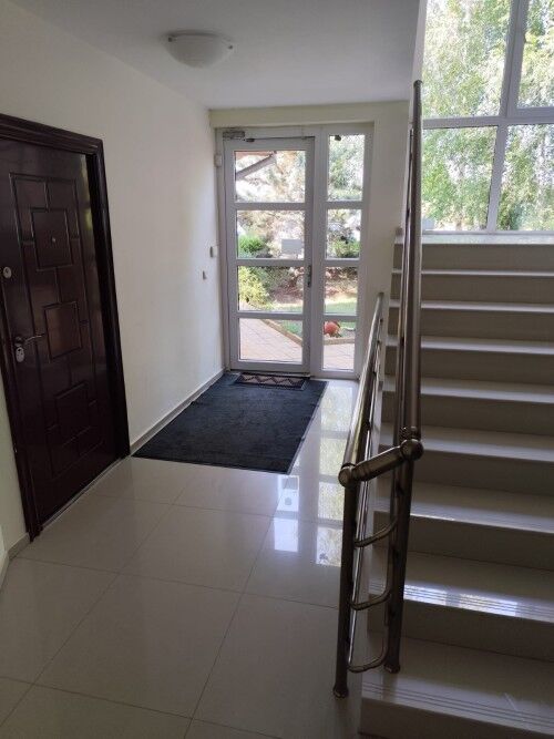 Bright entrance hall with staircase and glass door leading outside.