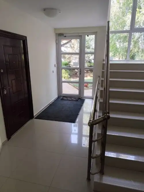 Bright entrance hall with staircase and glass door leading outside.