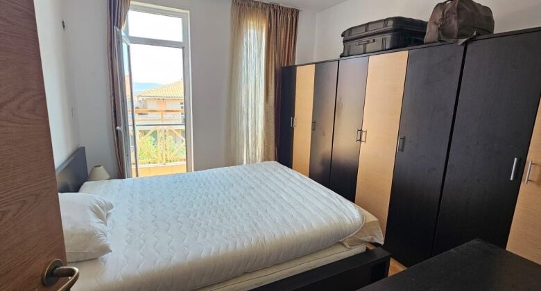 Bright bedroom with wardrobe, large window, and balcony overlooking scenic surroundings.