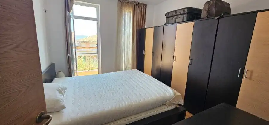 Bright bedroom with wardrobe, large window, and balcony overlooking scenic surroundings.