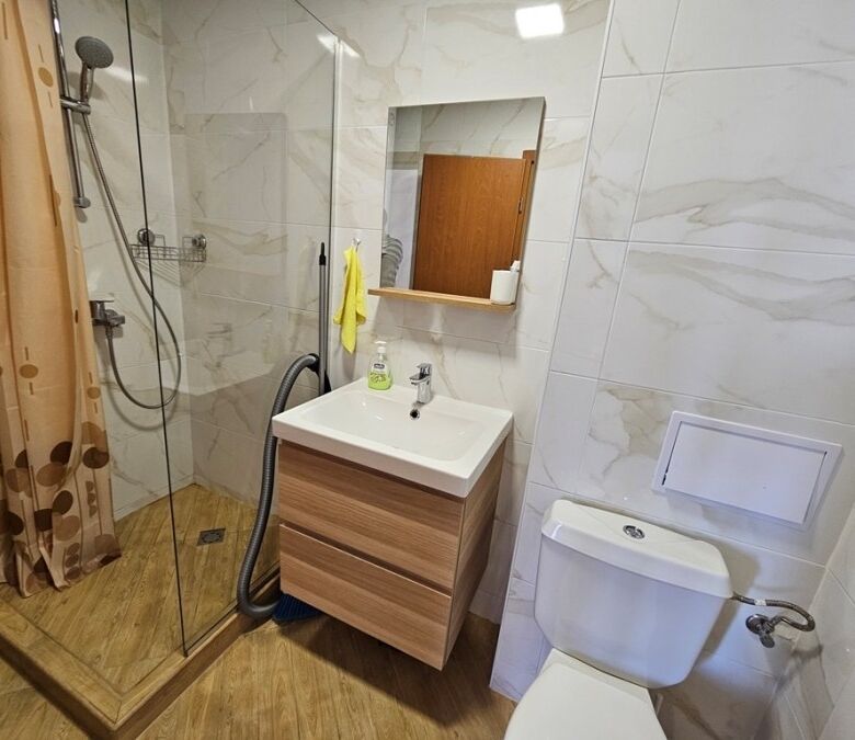 Bright bathroom with shower, sink, and toilet in a compact studio apartment.