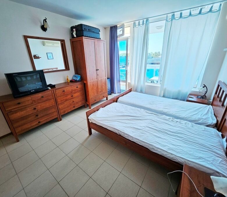 Sea view hotel room with twin beds, wardrobe, and TV.