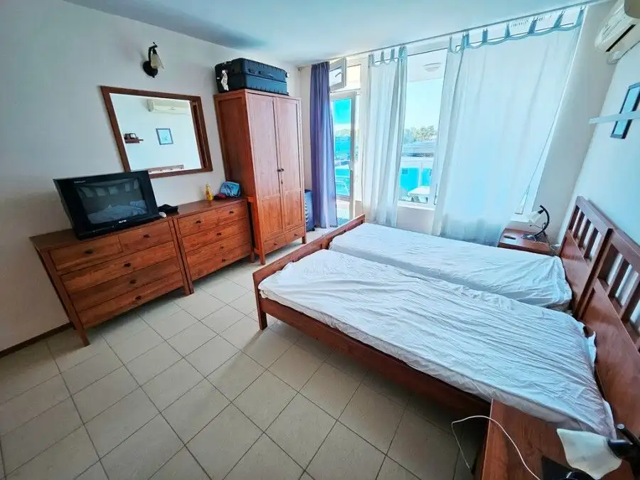 Sea view hotel room with twin beds, wardrobe, and TV.