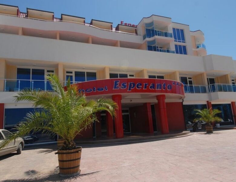 Esperanto hotel front view with palm trees and parking area.
