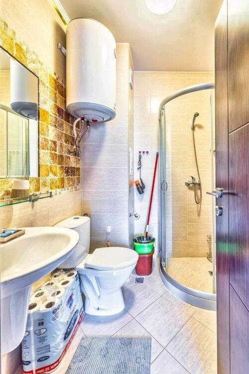 Bright bathroom with shower, toilet, and water heater in a compact space.