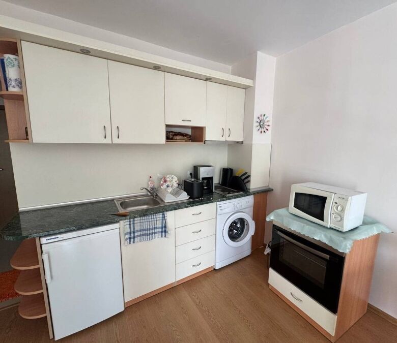 Bright kitchen with white cabinetry, washing machine, microwave, and oven in a coastal apartment.