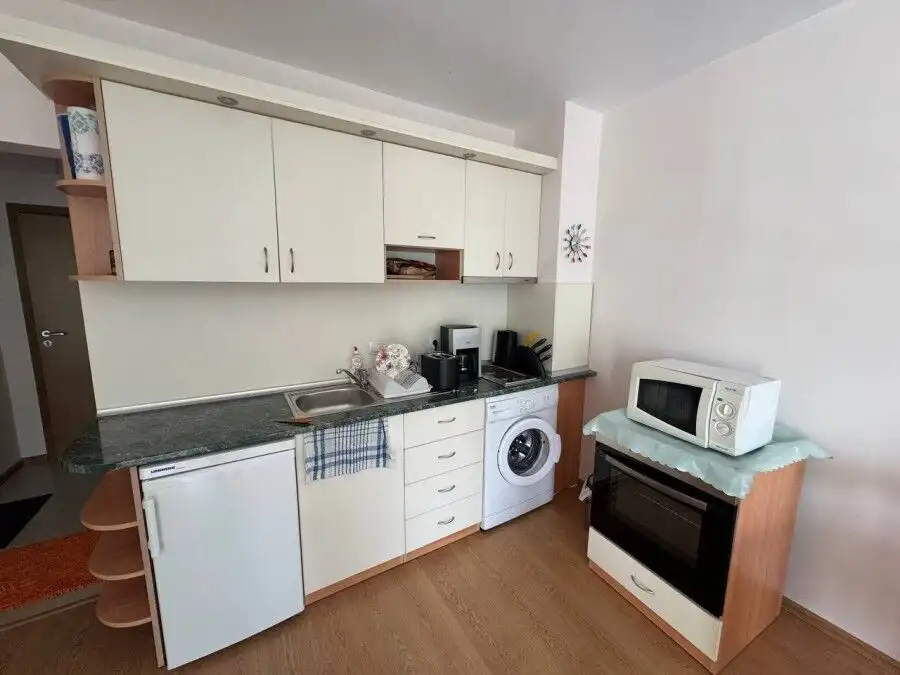 Bright kitchen with white cabinetry, washing machine, microwave, and oven in a coastal apartment.