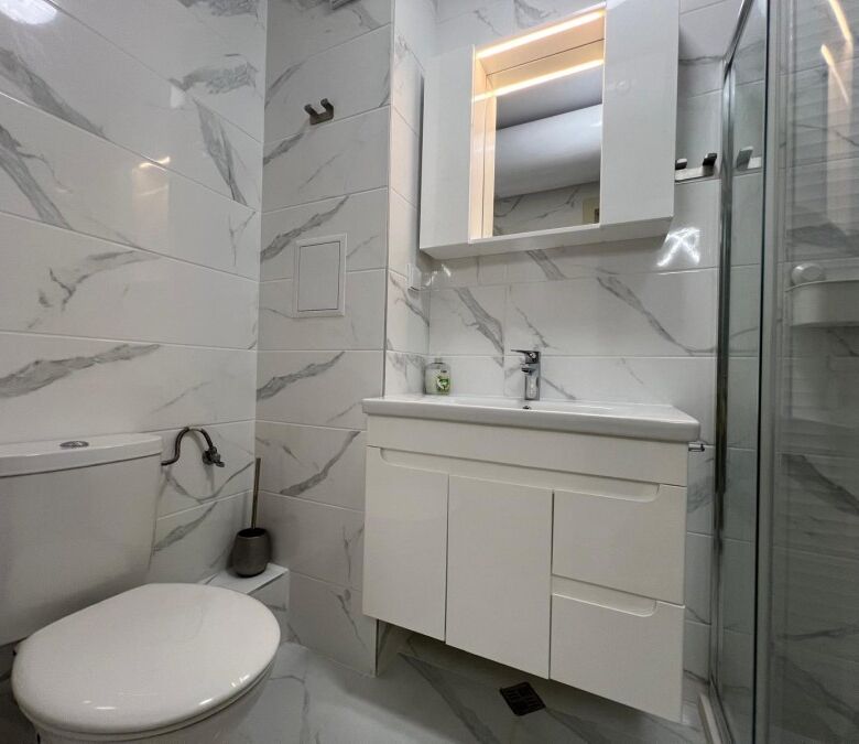 Bathroom with white marble tiles, modern sink, and mirror in top-class complex Valencia Gardens, Nes.