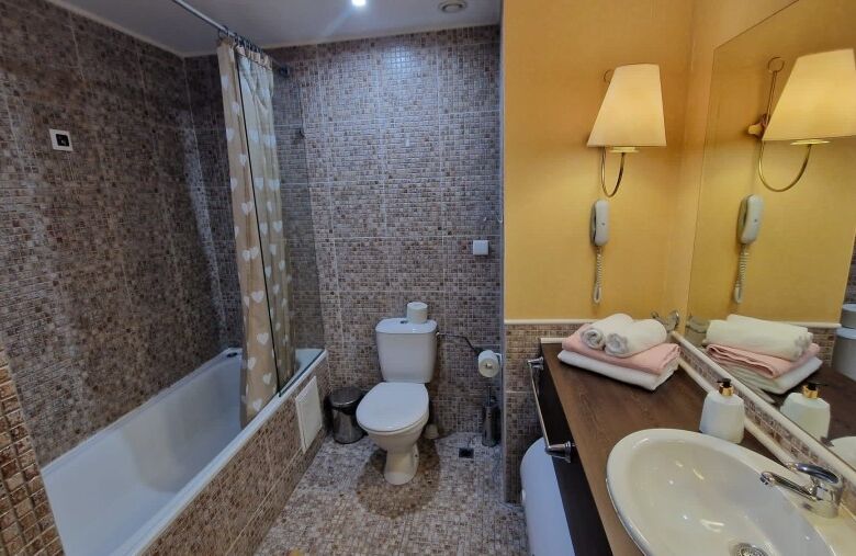 Bathroom with bathtub, toilet, and beige mosaic tiles in a stylish apartment.