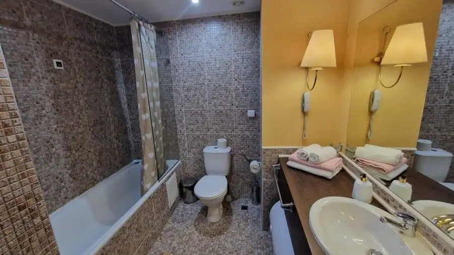 Bathroom with bathtub, toilet, and beige mosaic tiles in a stylish apartment.